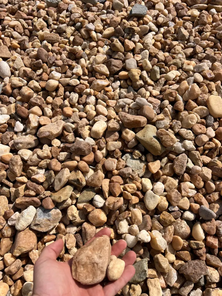 Hand holding rounded river rocks over a pile of tan and white gravel.