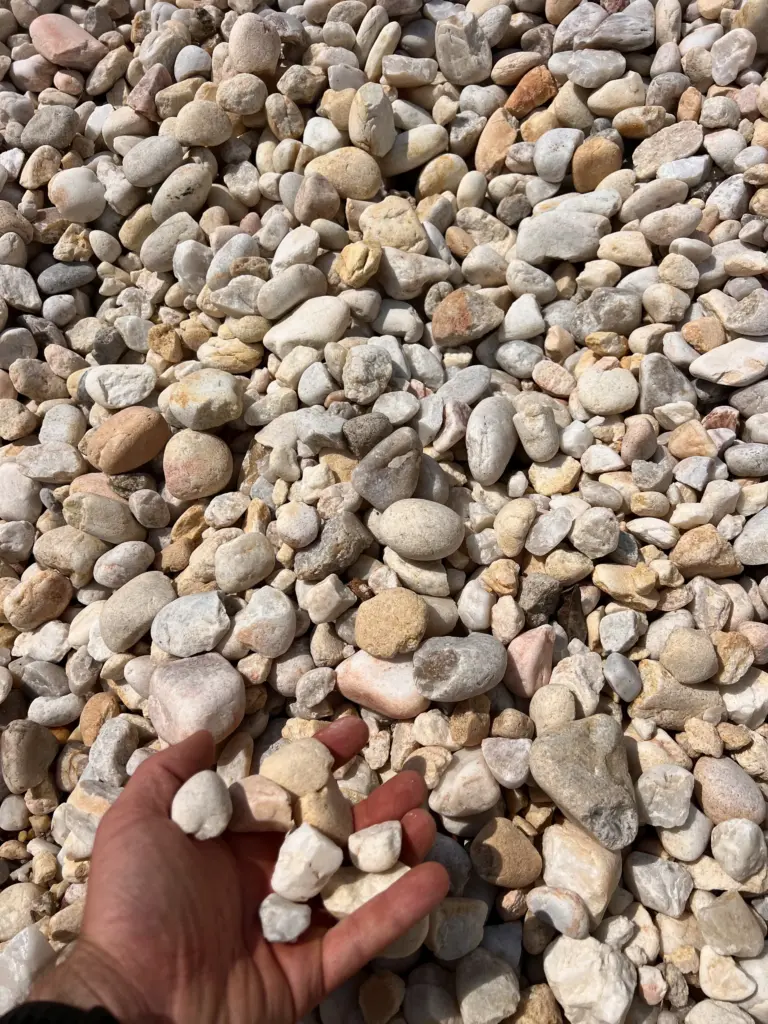 Hand holding white river rock over a pile of rounded stones.