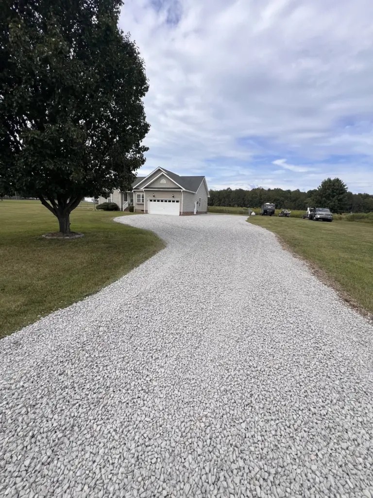 Curved gravel driveway leading to a single-story house with attached garage on a large lawn.