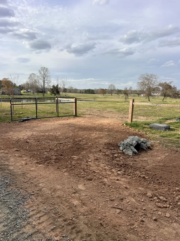 Freshly graded dirt driveway entrance by a farm gate with a small rock pile in Gallatin, Tennessee.