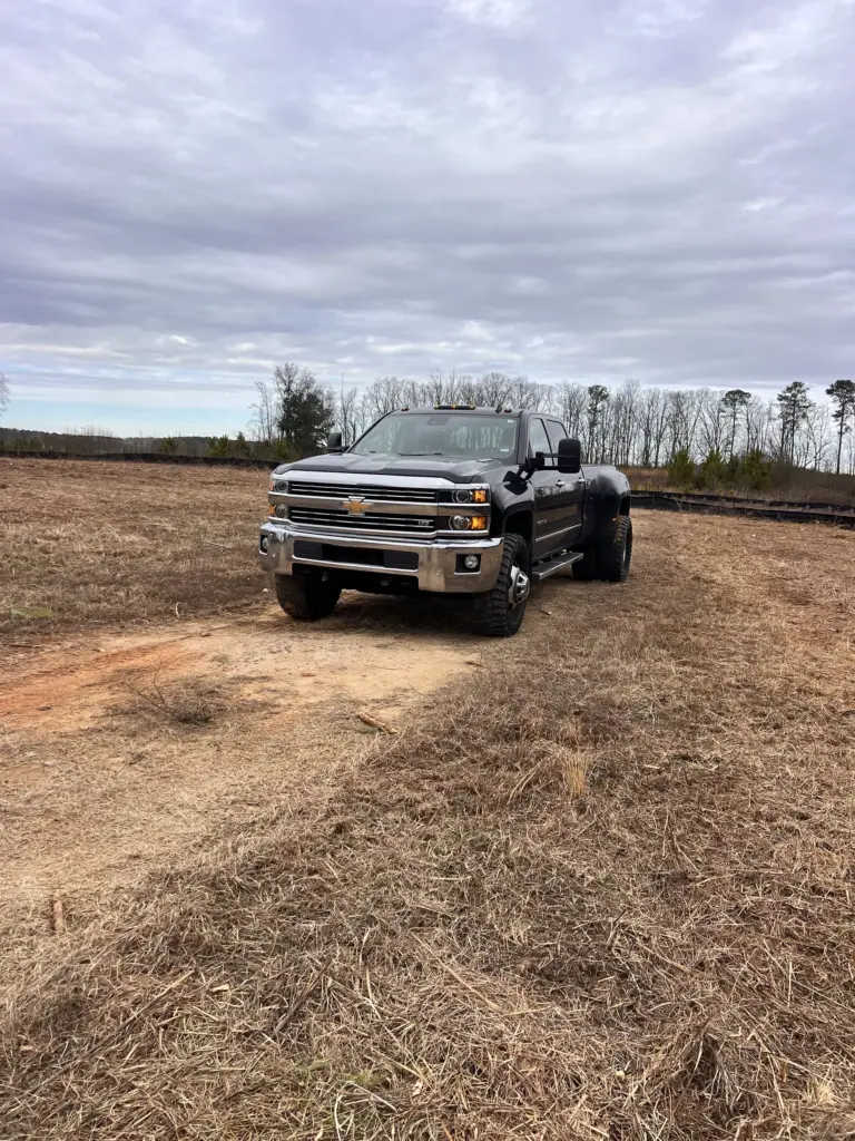 Black dually pickup truck parked on a cleared field with trees in the background.