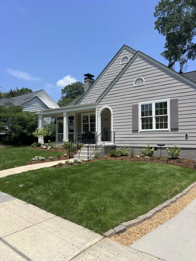 Freshly sodded front yard with flower beds, stone edging, and a gray house with porch and steps.