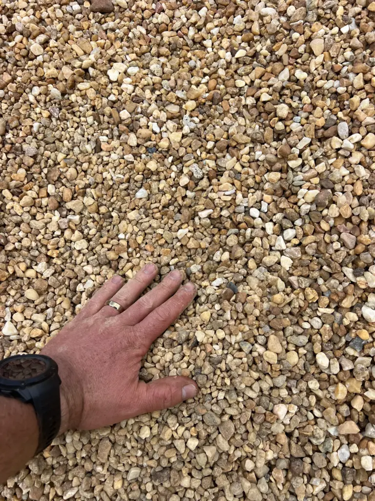 Hand resting on small pea gravel stones in a close-up view.
