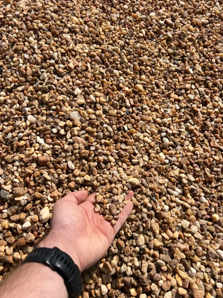 Hand scooping pea gravel stones from a large pile