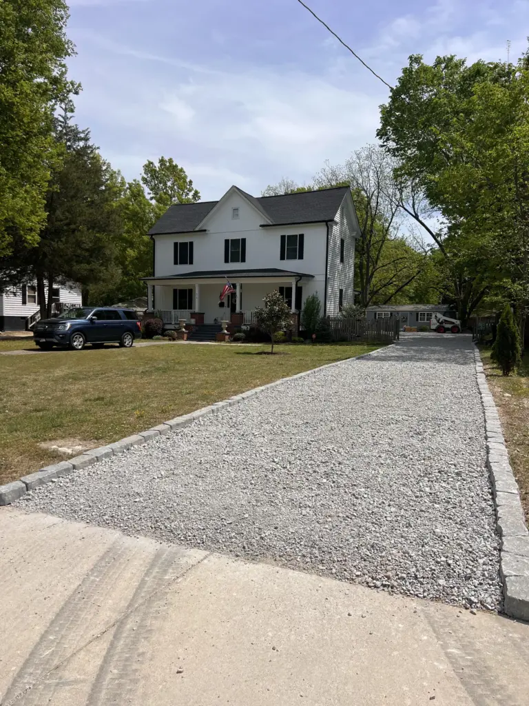 Long gravel driveway with stone edging leading to a white two-story house and lawn.