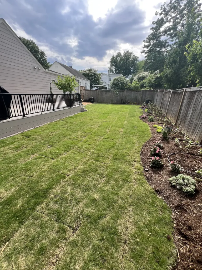Freshly sodded backyard with mulch flower bed, wooden privacy fence, and a raised deck.