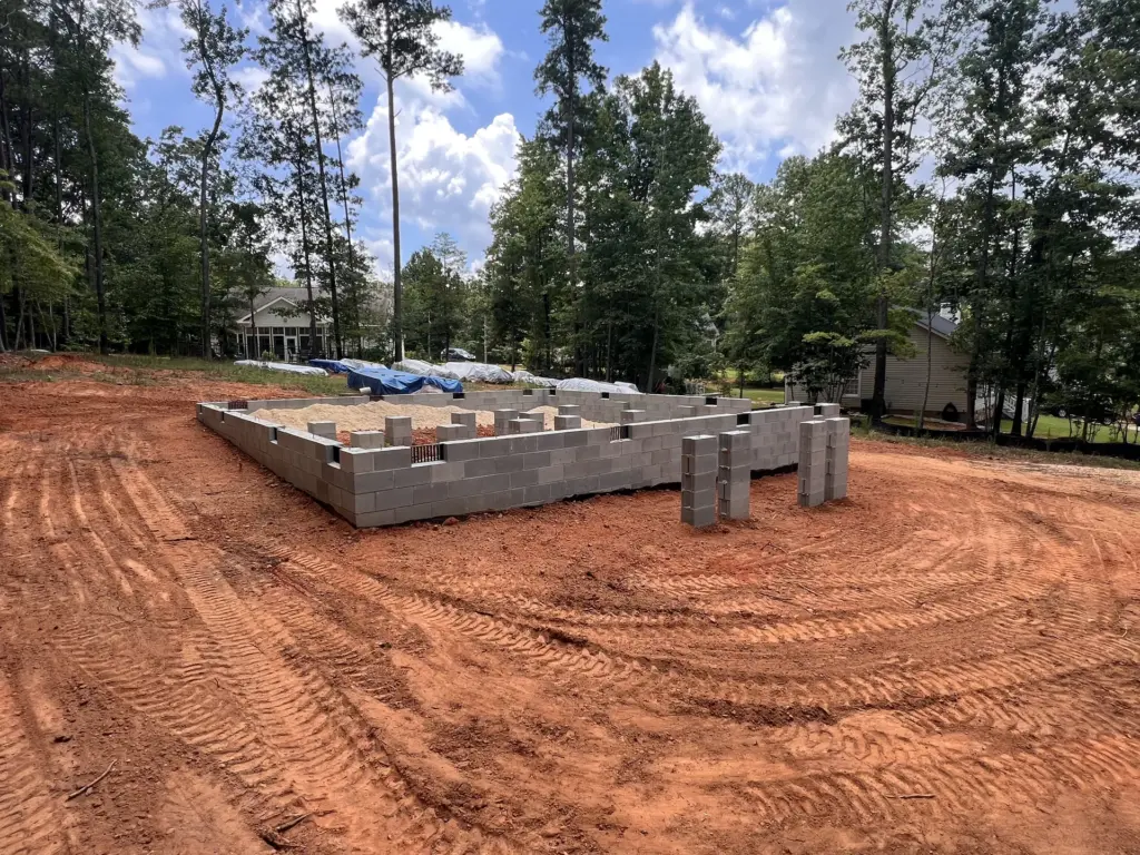 Concrete block foundation on a graded red clay homesite, with wooded neighborhood in the background.