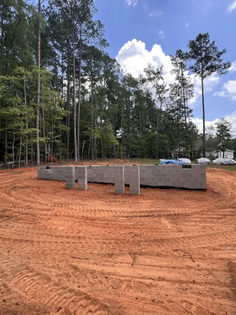 CMU stem wall foundation on cleared red clay lot, Sumner County, TN, with surrounding trees.