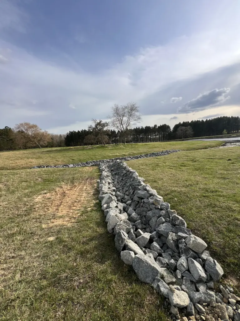 Rock-lined drainage swale in a grassy field forming a Y-shaped channel for stormwater control.