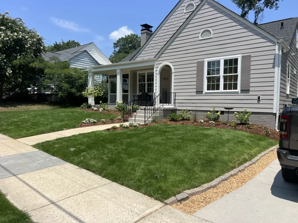 Freshly landscaped front yard with new sod, mulched beds, stone edging, and a gray bungalow with porch.